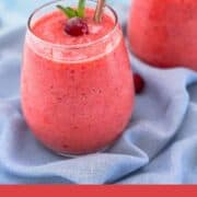 Two glasses of cranberry smoothie on a blue cloth, blended with fresh or frozen cranberries for a vibrant color and creamy texture. Healthy cranberry smoothie recipe made with clementines, banana, and pineapple.
