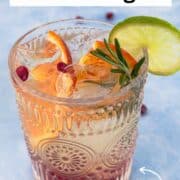 Easy White Sangria in a patterned glass with ice, sliced blood orange, pomegranate seeds, lime, and a fresh rosemary garnish. Light and refreshing white wine sangria perfect for holiday gatherings or winter parties. Bright citrus-forward cocktail on a cool blue background.