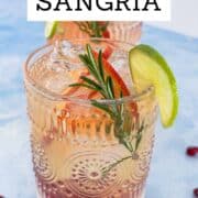 White Wine Sangria served in a textured glass filled with ice, blood orange slices, lime, fresh rosemary, and pomegranate seeds. A bright and refreshing white sangria cocktail styled for fall and winter gatherings. Overhead close-up with vibrant citrus and festive garnishes.