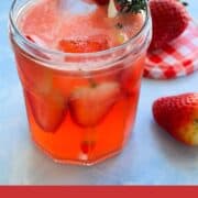 Close-up of a refreshing gin and jam cocktail made with strawberry jam, lemon juice, and tonic water, served over ice in a small glass jar and garnished with fresh strawberries and thyme.
