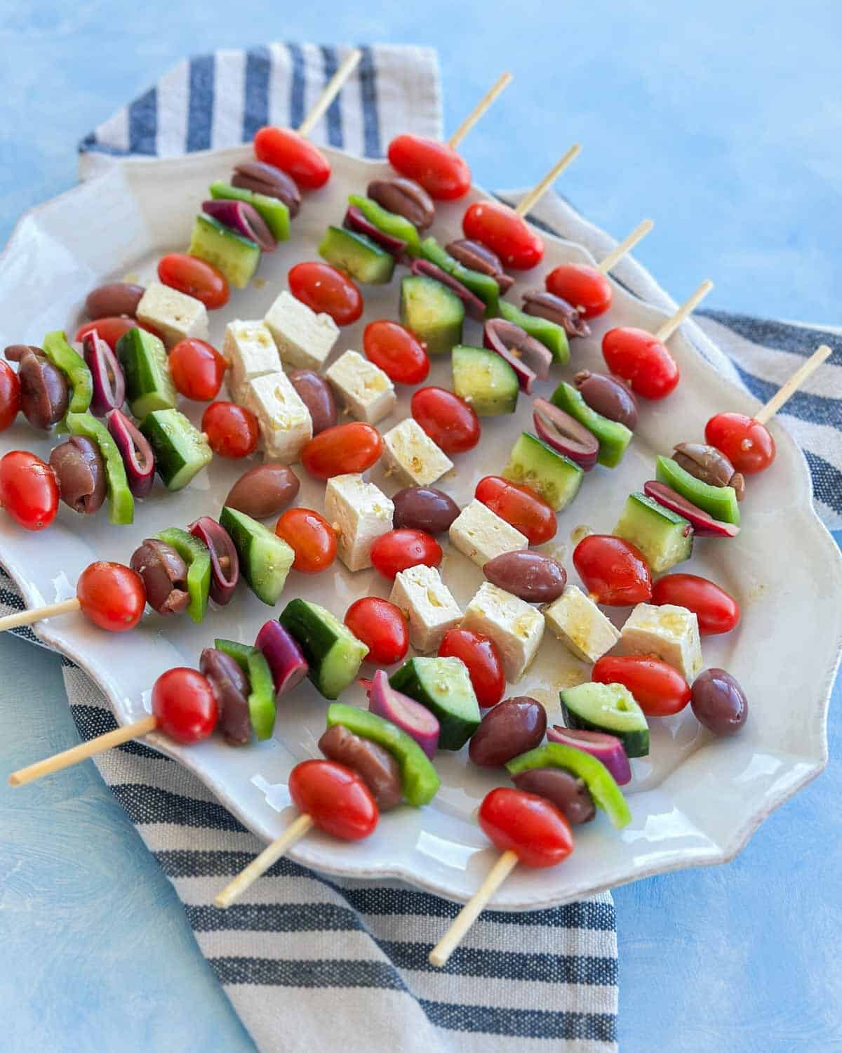 Greek salad skewers with feta, cucumber, tomatoes, olives and red onion served as an easy Mediterranean appetizer on a white platter.