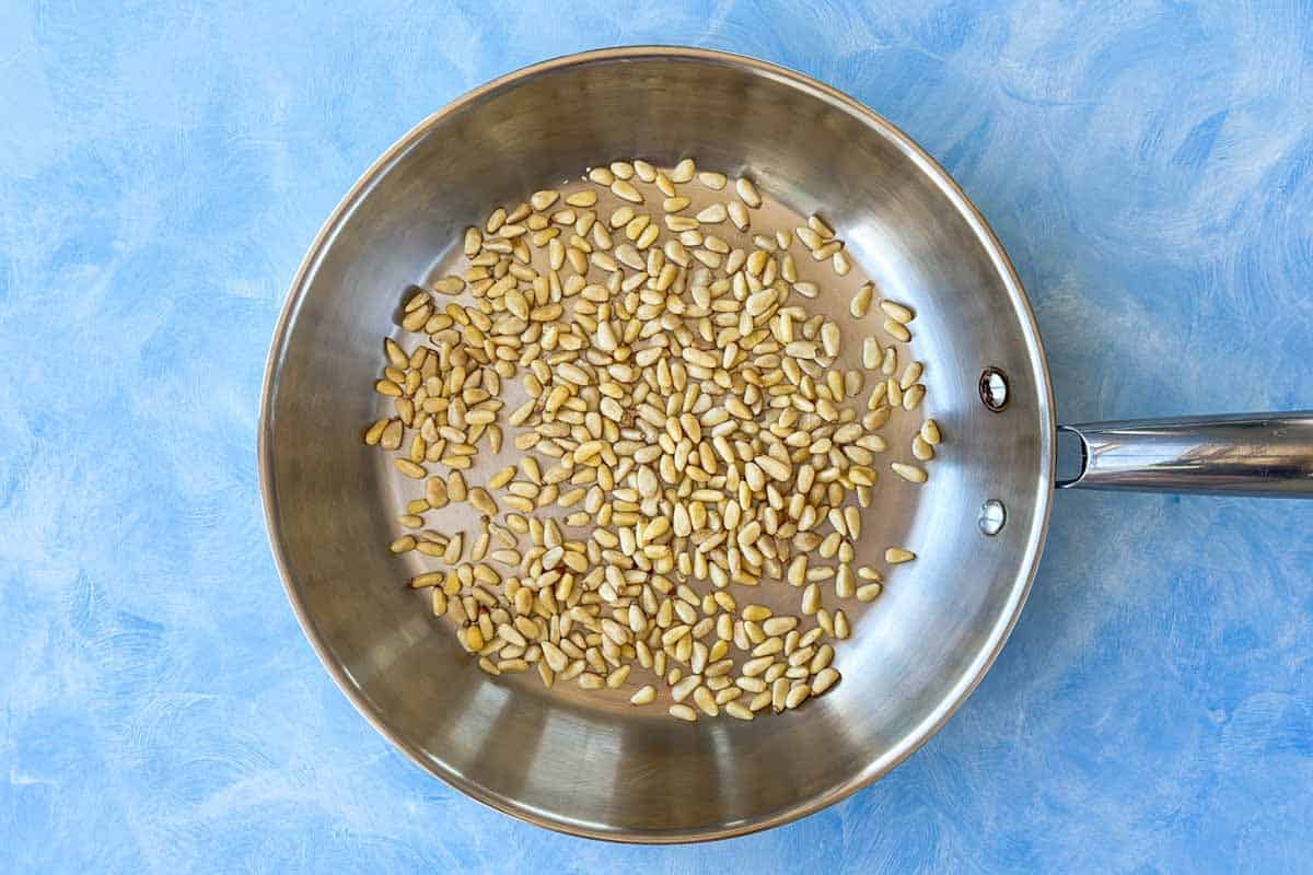 Raw pine nuts scattered in a stainless steel skillet, ready to toast on the stove.