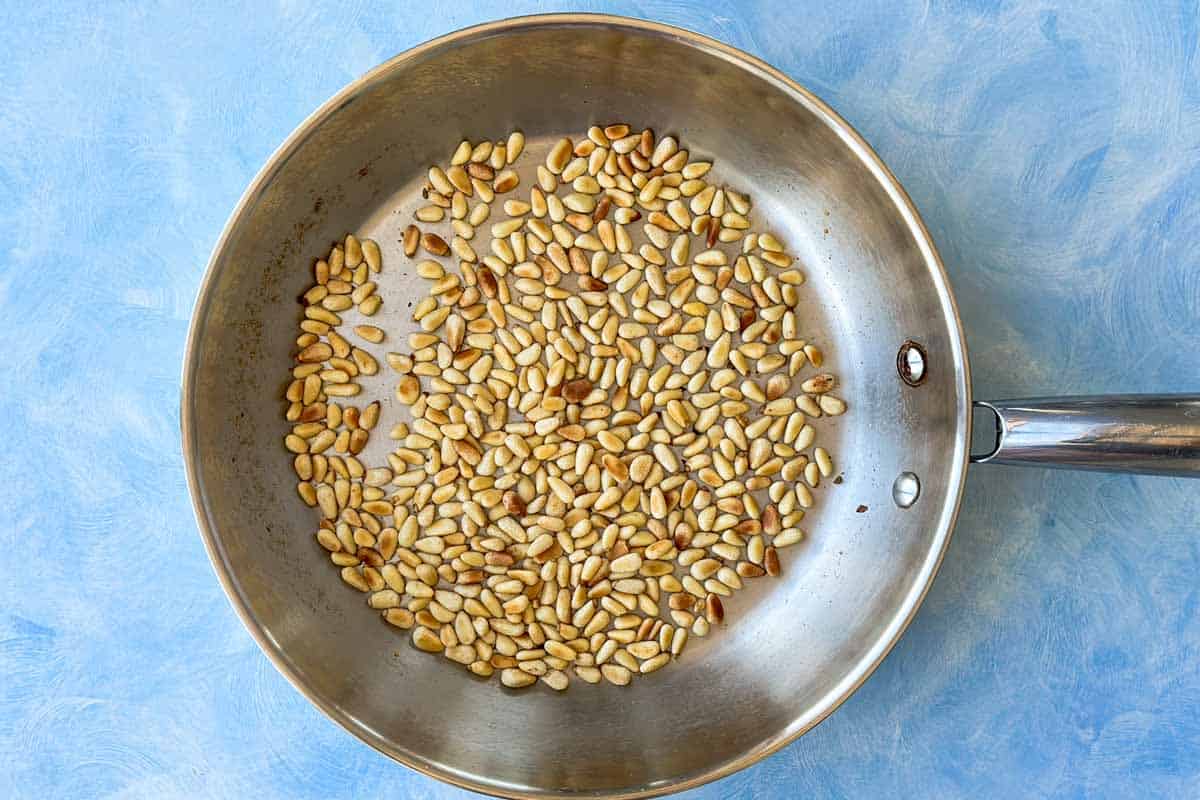Pine nuts toasted in a stainless steel skillet until golden with lightly browned edges.