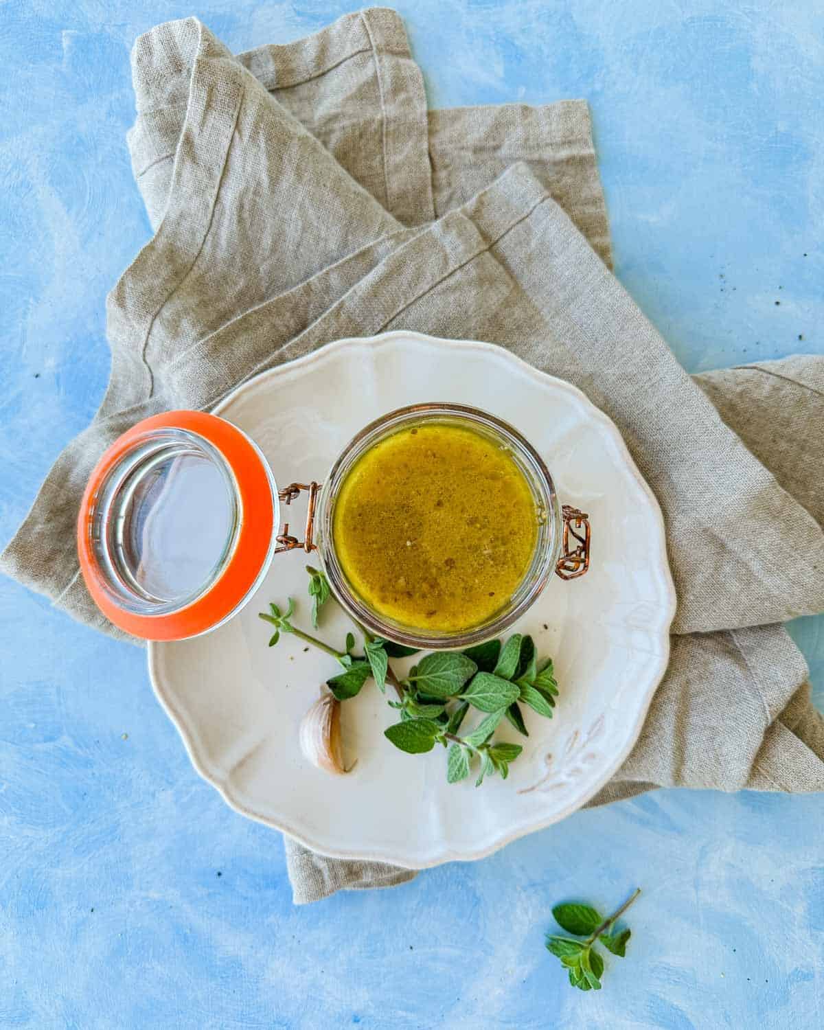 Overhead shot of red wine vinegar dressing in an open glass jar, styled with fresh herbs, garlic, and a rustic linen cloth.