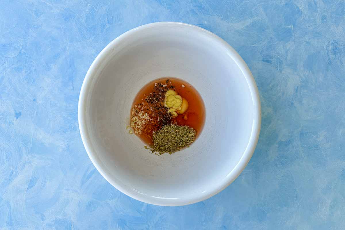Red wine vinegar, Dijon mustard, garlic, dried oregano, salt, and pepper combined in a bowl, ready to be whisked into a dressing.