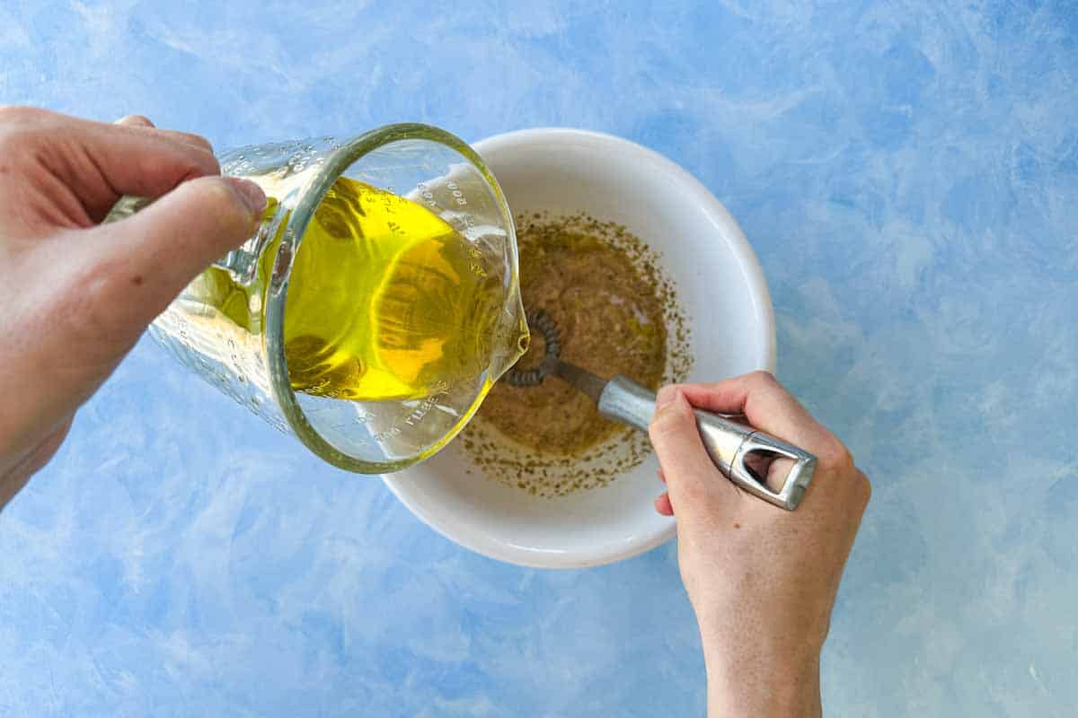 Olive oil being slowly poured into a bowl while whisking, creating a smooth and emulsified red wine vinegar dressing.
