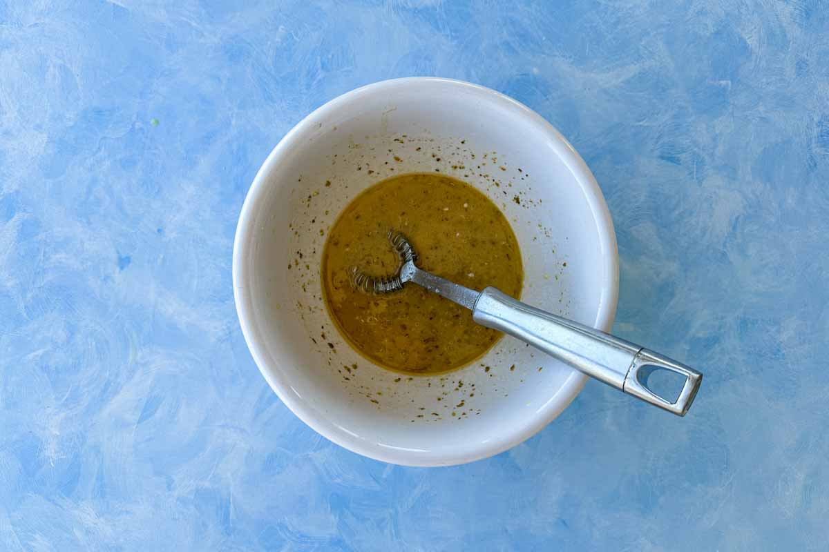 Finished red wine vinegar dressing in a bowl with a whisk, showing a well-emulsified, glossy texture ready to serve.