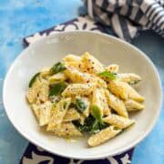 Creamy ricotta and lemon pasta plated in a white bowl with fresh basil leaves, parmesan cheese, and chili flakes on a light blue background.
