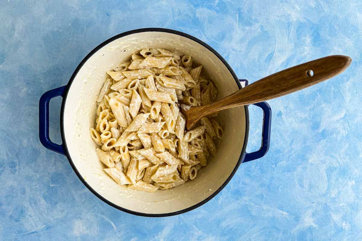 Cooked penne pasta tossed with creamy ricotta sauce in a Dutch oven, creating a smooth and velvety coating.