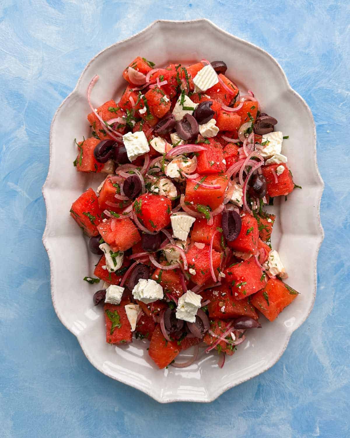 Overhead composition of watermelon feta salad arranged on a platter with bright colors and fresh Mediterranean-style ingredients.