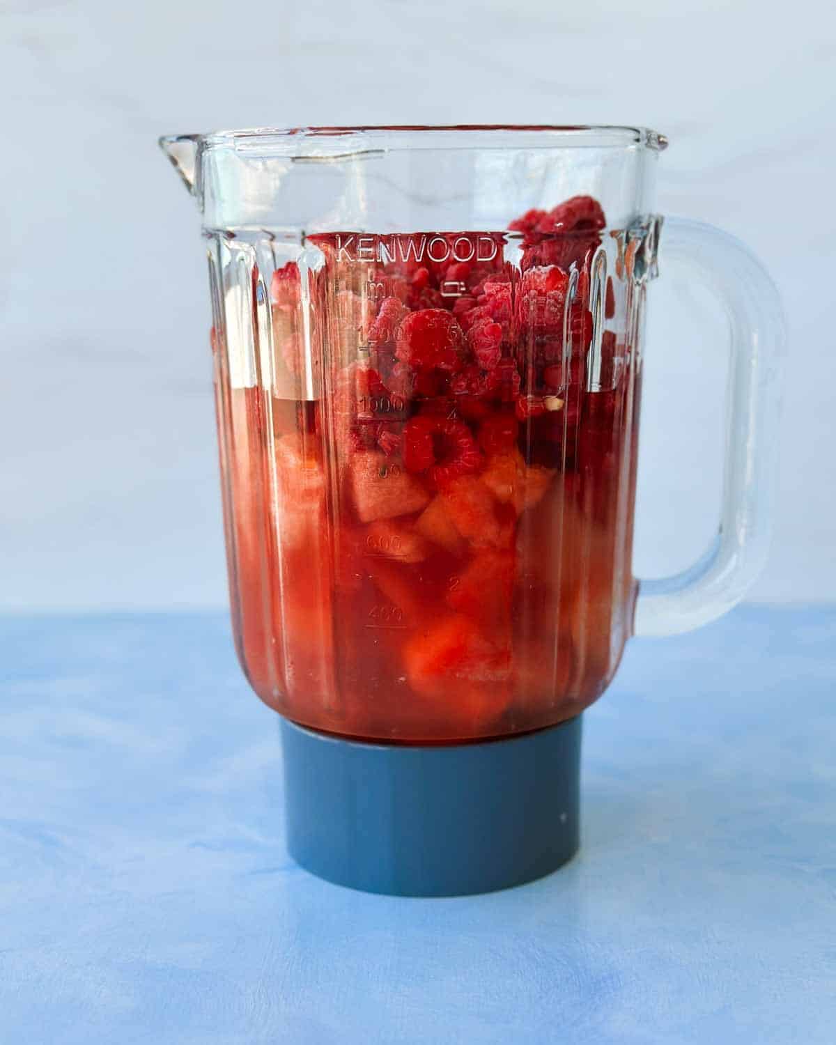 Blender jug filled with watermelon chunks, frozen raspberries, and rosé wine ready to make homemade watermelon frosé.