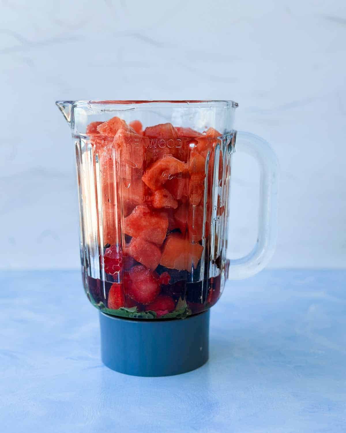 Blender filled with watermelon chunks, frozen berries, fresh mint, and lemon juice ready to make a watermelon slushie
