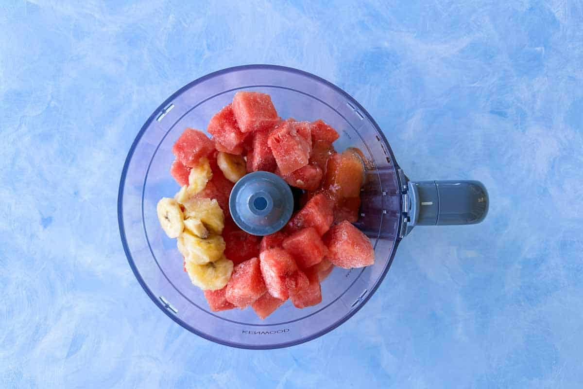 Frozen watermelon chunks and sliced banana in a food processor bowl, ready to be blended into homemade watermelon sorbet.