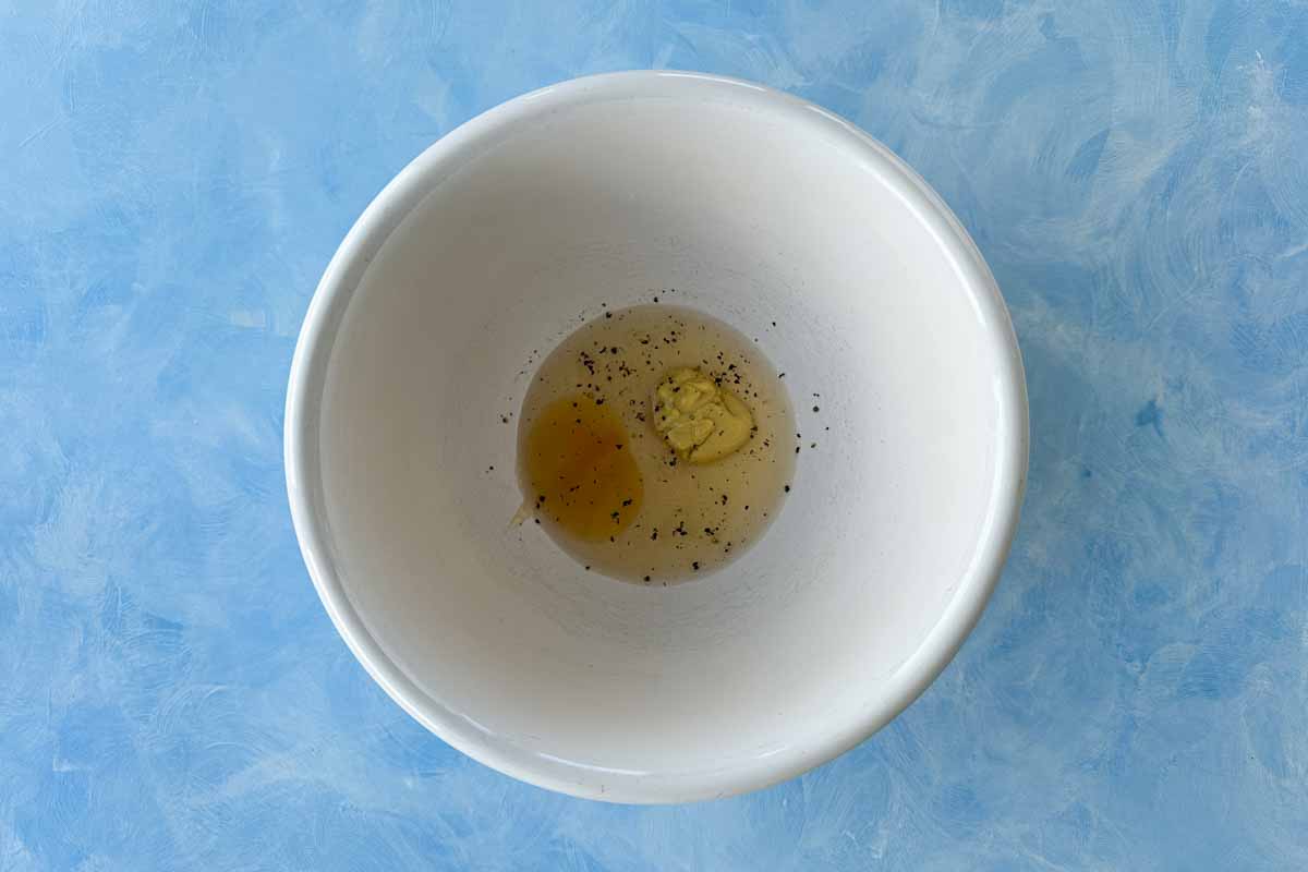 White wine vinegar, Dijon mustard, honey, salt, and pepper in a white bowl ready to be whisked together to start the vinaigrette.