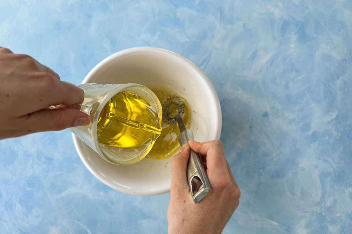 Olive oil being poured into a bowl while whisking to emulsify the white wine vinaigrette.