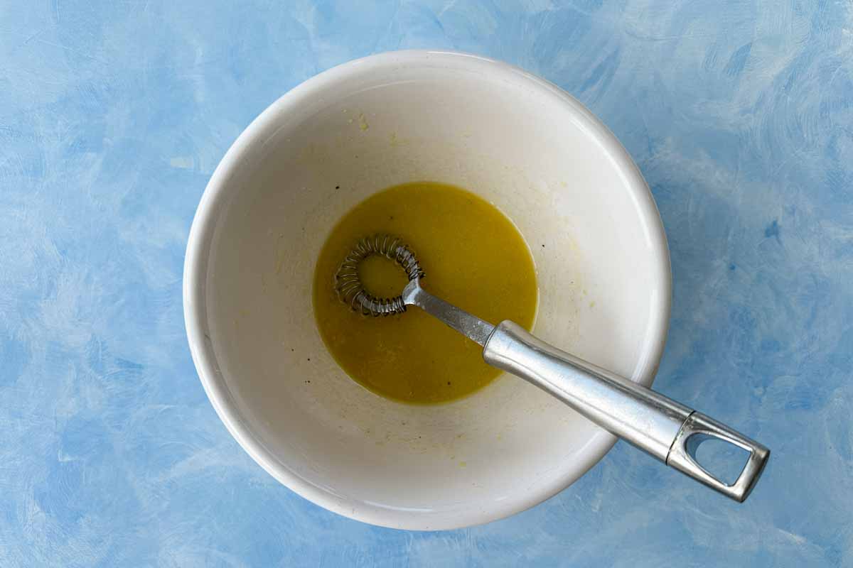 Freshly whisked white wine vinaigrette in a bowl with a small whisk resting inside.