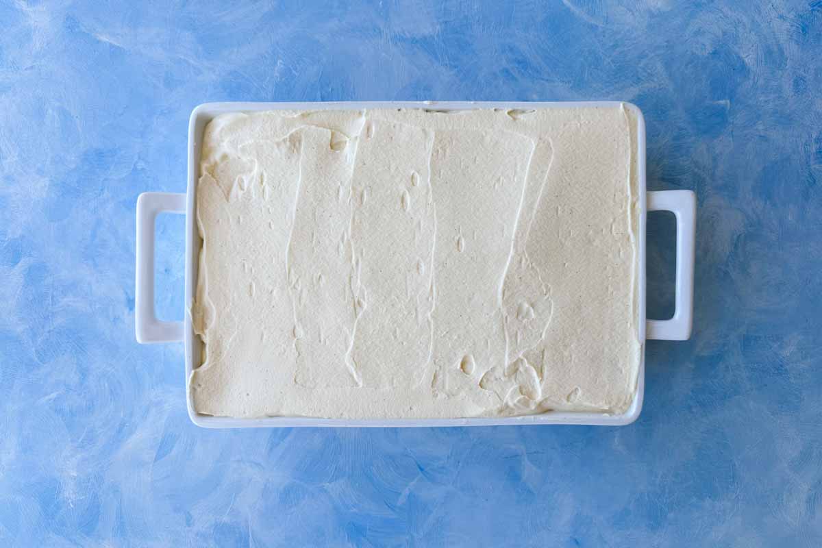 Top view of a baking dish fully covered with a smooth, even layer of mascarpone cream, ready for the final topping.