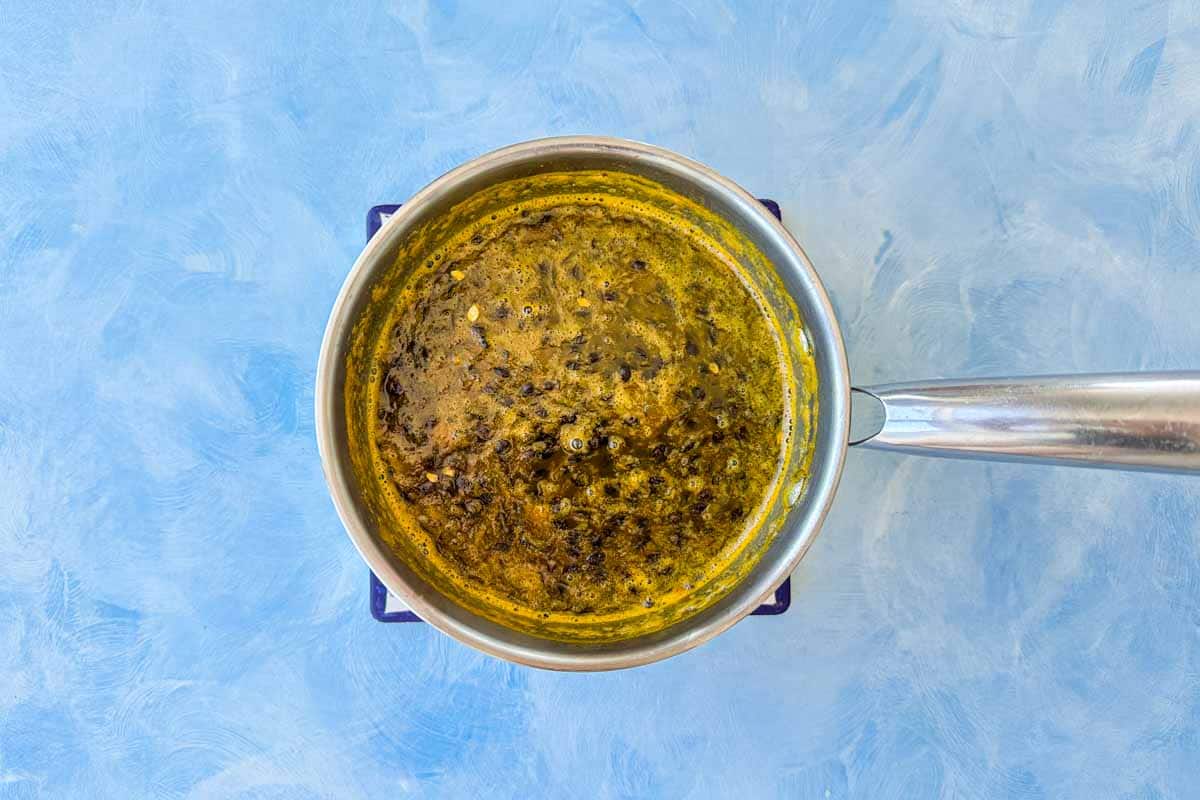 Top-down view of passion fruit mixture simmering in a saucepan, with the pulp darkening and thickening as it cooks, showing bubbles and reduced texture.