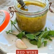 Jar of homemade vinaigrette with herbs and garlic on a white plate.
