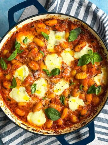Top view of baked gnocchi arrabbiata in a skillet with melted bocconcini, fresh basil, and rich tomato sauce.