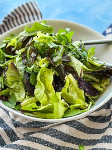 Angled view of a bistro salad with tender mixed leaves, parsley, and chives in a white serving bowl.