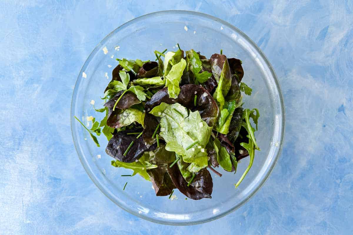 Top view of bistro salad after tossing, with mixed greens and fresh herbs lightly coated in vinaigrette.