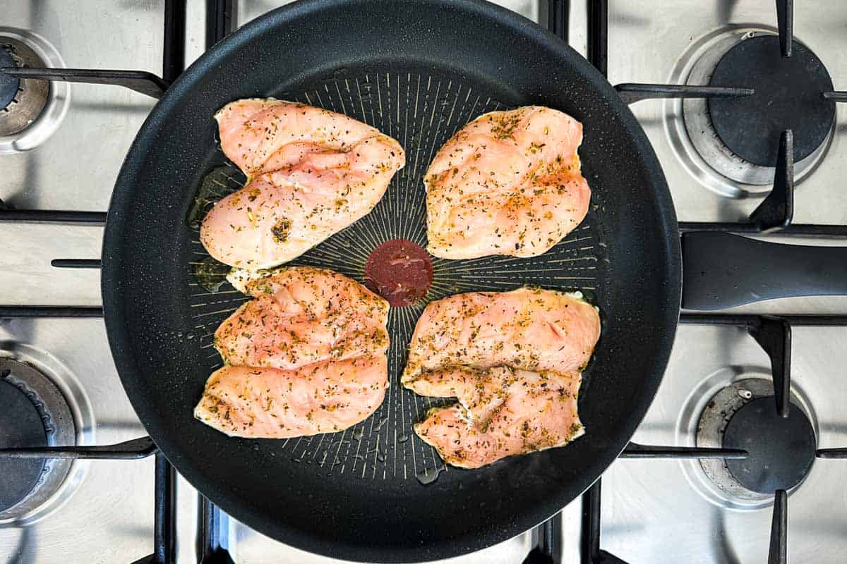 Seasoned chicken breasts placed in a black skillet, ready to cook on the stovetop.