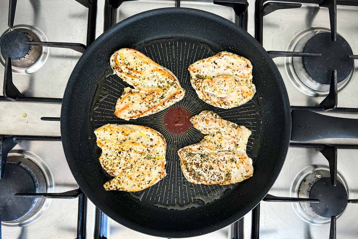 Chicken breasts searing in a skillet until lightly golden and cooked through.