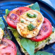 Close-up view of a pesto caprese sandwich with creamy mozzarella, ripe tomato, basil leaves, and glossy balsamic glaze.