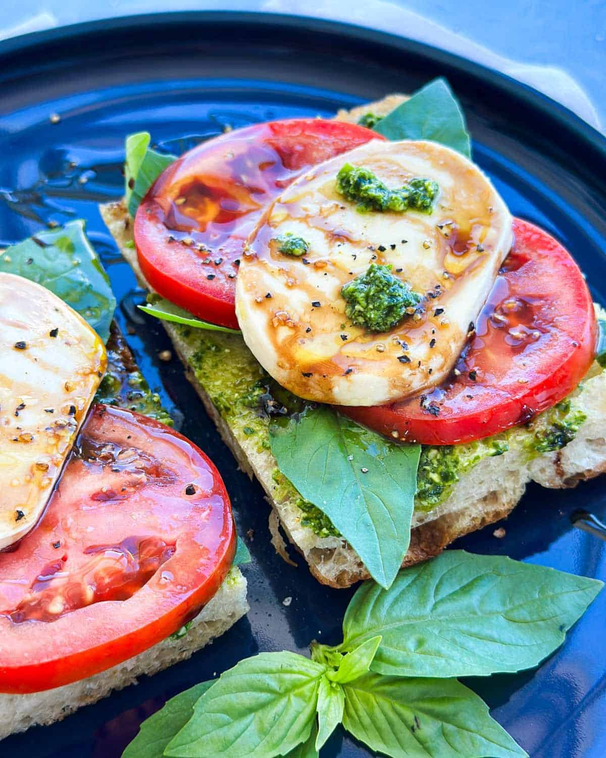 Detailed close-up of a pesto caprese sandwich with fresh tomato, mozzarella, basil, pesto, and balsamic glaze