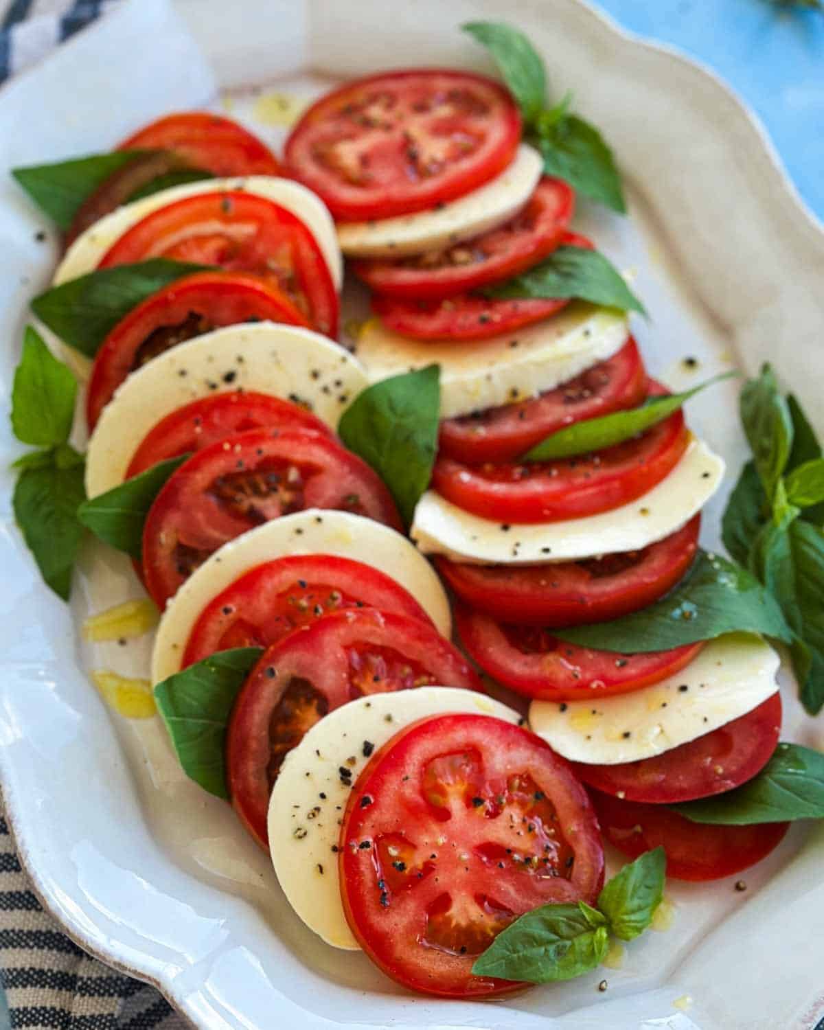 Close-up detail of caprese salad focusing on the texture of ripe tomatoes, smooth mozzarella slices and fresh basil, with olive oil pooling lightly on the plate.