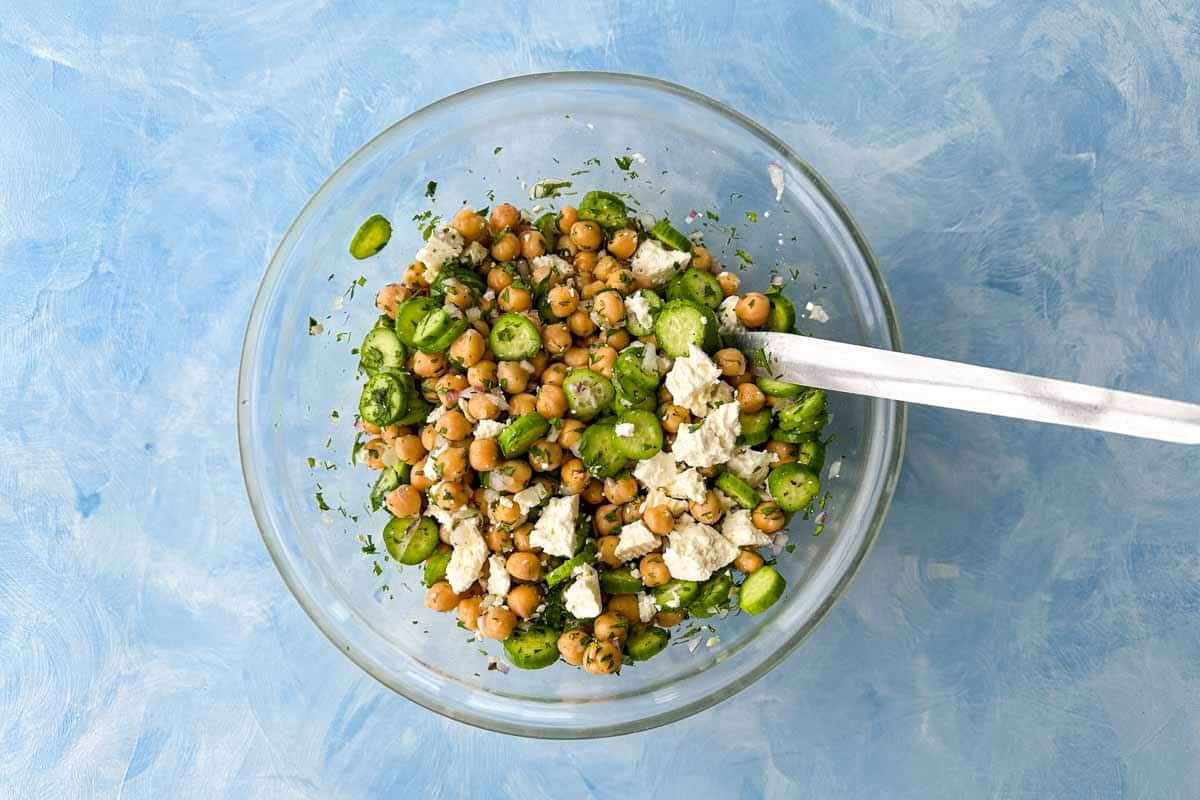 Chickpea and feta salad ingredients tossed together with cucumber, herbs, red onion, and crumbled feta.