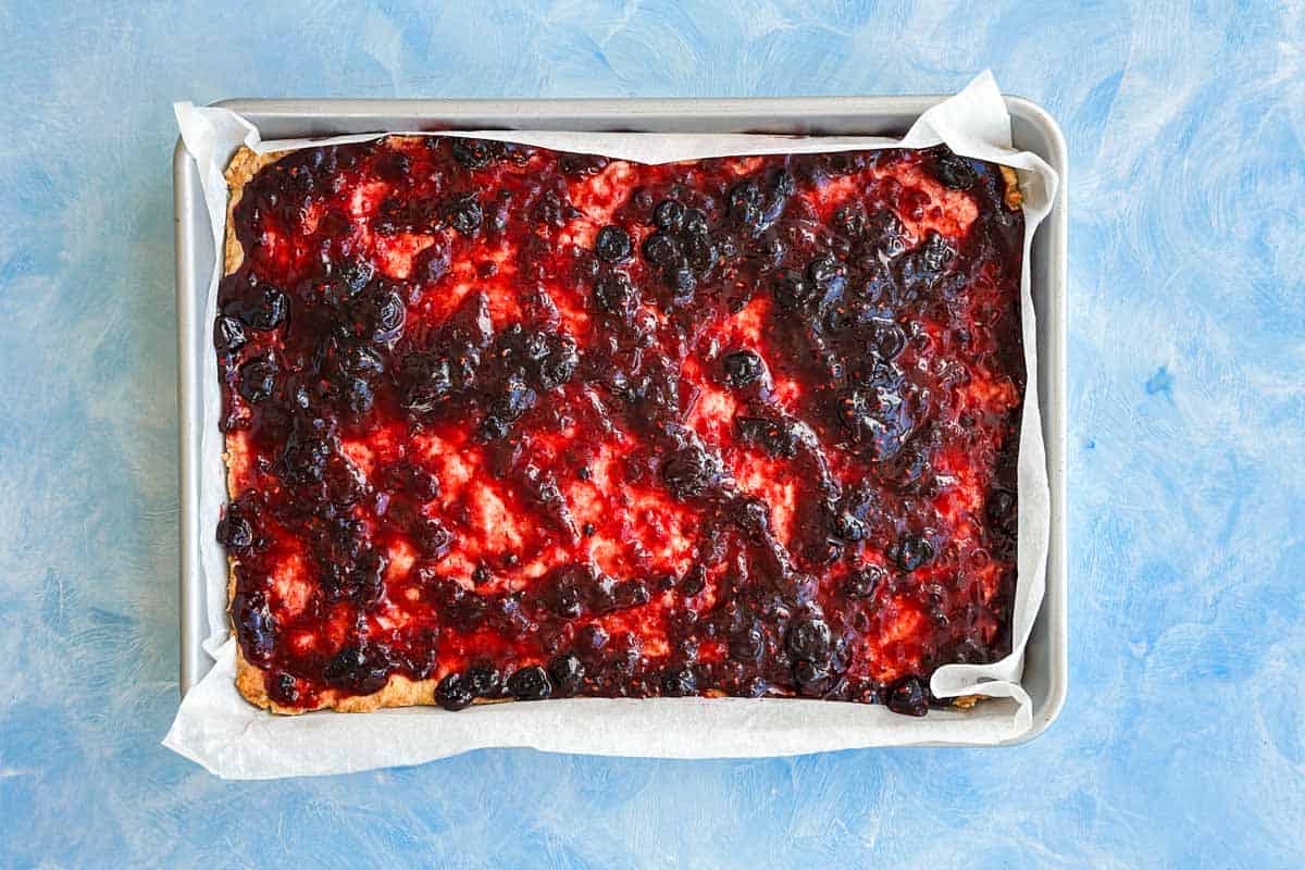 Mixed berry jam spread evenly over the baked shortbread base before adding the berry layer.