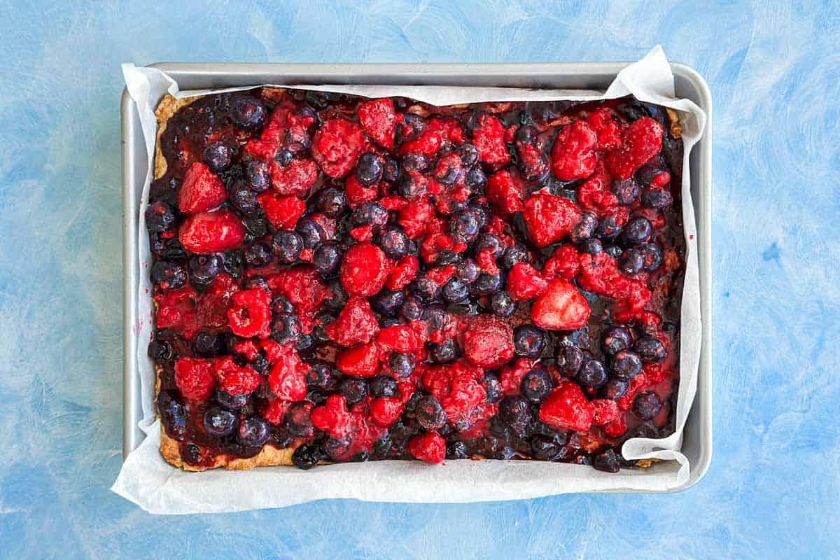 Fresh and frozen mixed berries scattered over the jam layer to create the filling for berry crumble bars