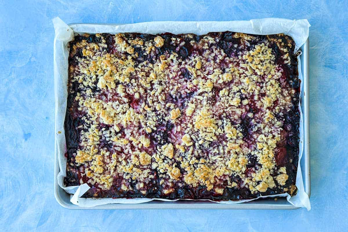Freshly baked berry crumble bars cooling in a baking tray with a golden crumble topping and bubbling berry filling.
