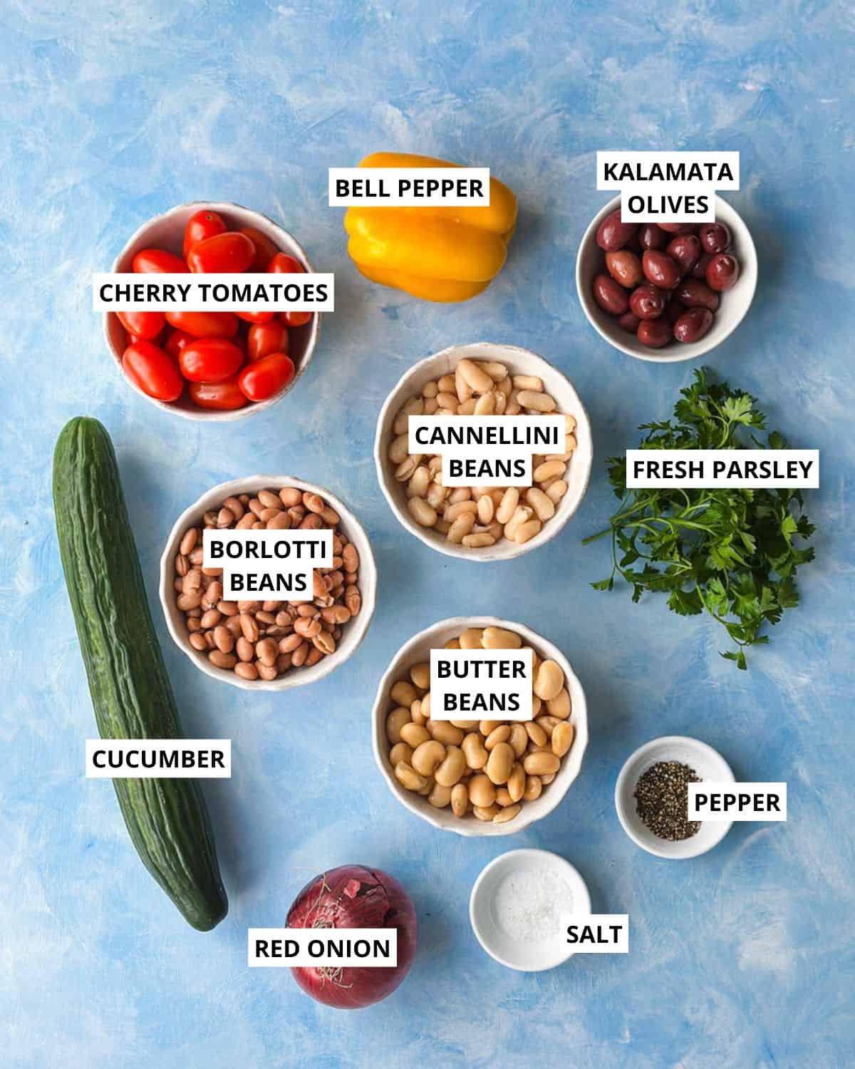 Ingredients for Italian dense bean salad including mixed beans, cherry tomatoes, cucumber, bell pepper, olives, parsley, and red onion.
