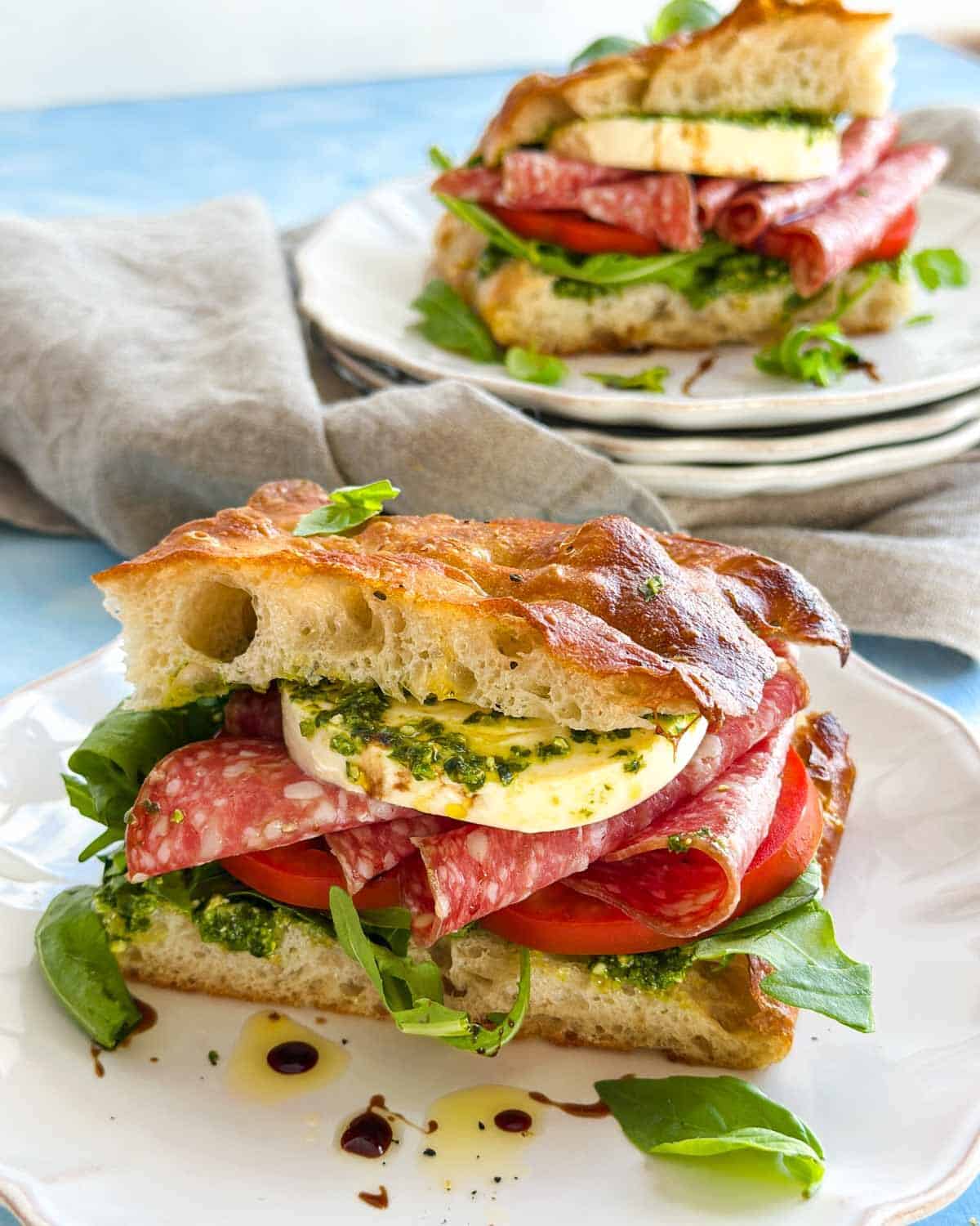 Side view of a focaccia bread sandwich with airy focaccia, pesto, fresh mozzarella, Italian salami and ripe tomatoes.