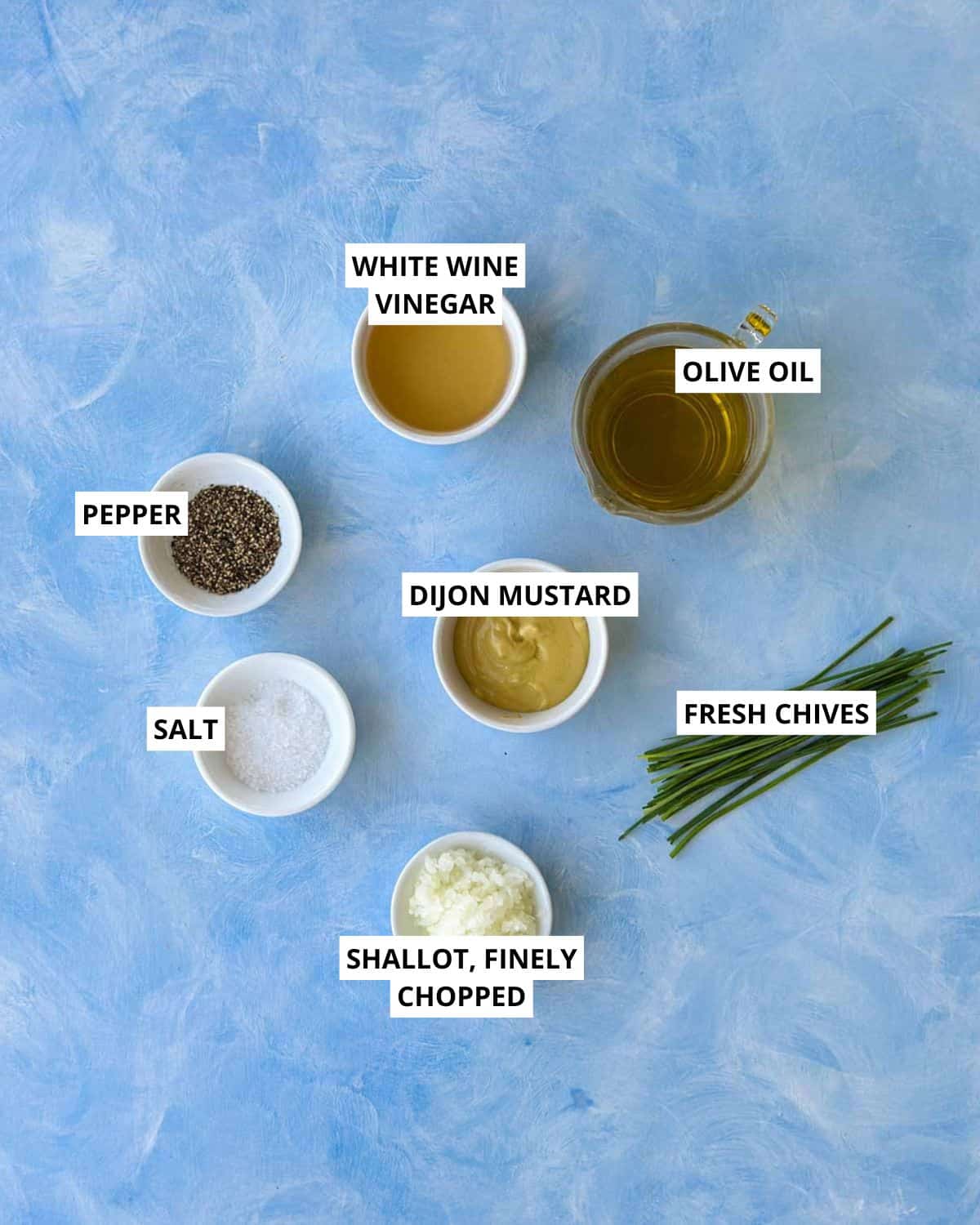 Top view of ingredients for classic French vinaigrette including olive oil, white wine vinegar, Dijon mustard, shallot, chives, salt, and pepper.