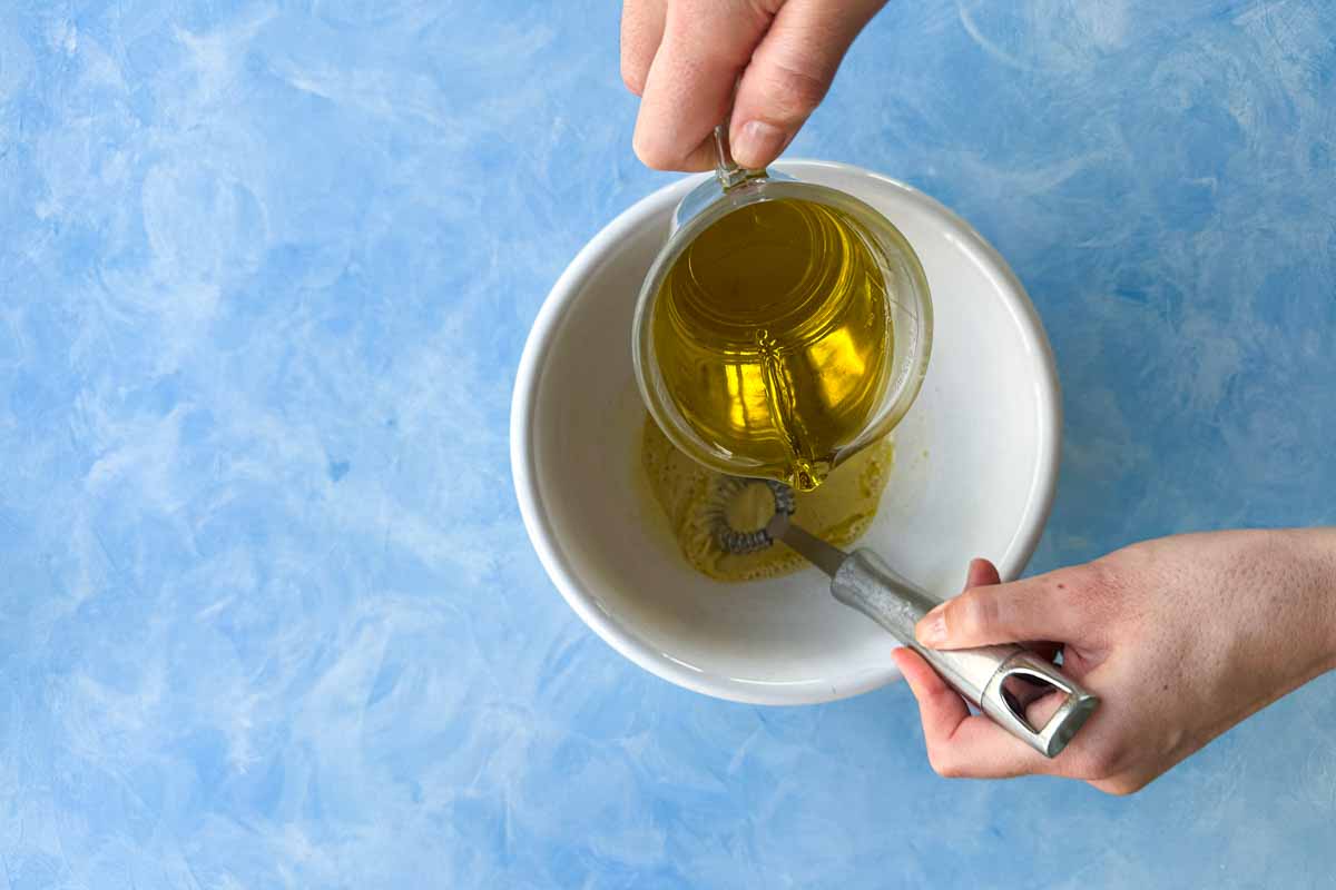 Top view of olive oil being poured into Dijon mustard and vinegar while whisking classic French vinaigrette.