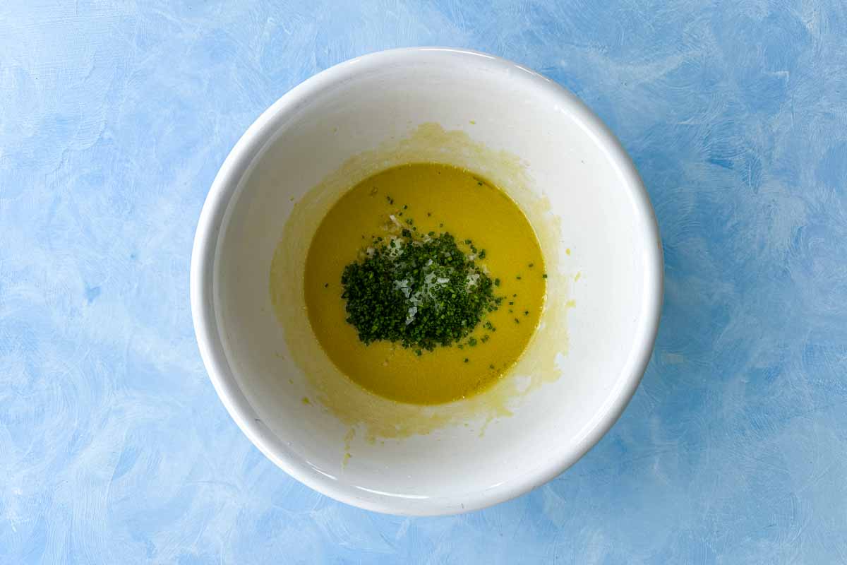 Top view of chopped chives and shallot added to classic French vinaigrette in a white mixing bowl.