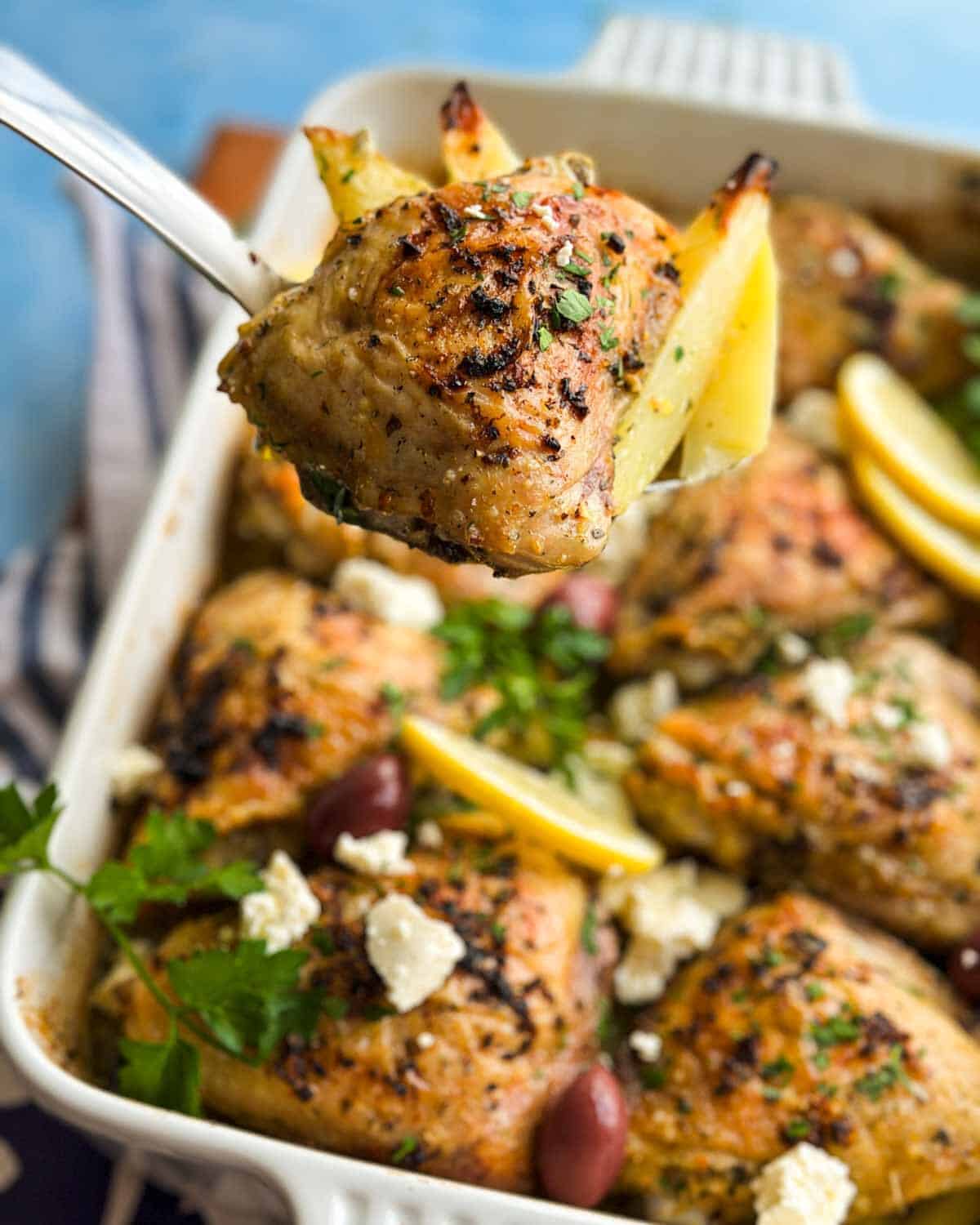 Close-up of a spoon holding roasted chicken and potato from Greek chicken and lemon potatoes with the baking dish blurred behind.