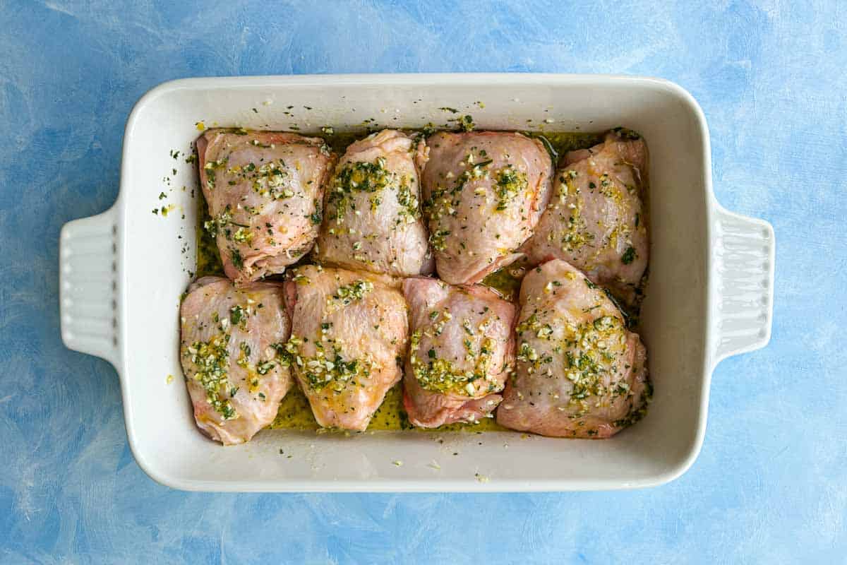 Top view of raw chicken thighs coated in lemon, garlic, and oregano marinade for Greek chicken and lemon potatoes.