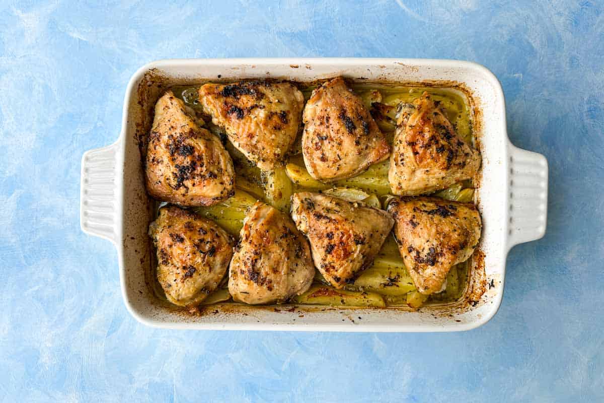 Top view of baked Greek chicken and lemon potatoes in a casserole dish before adding feta, olives, parsley, and lemon garnish.