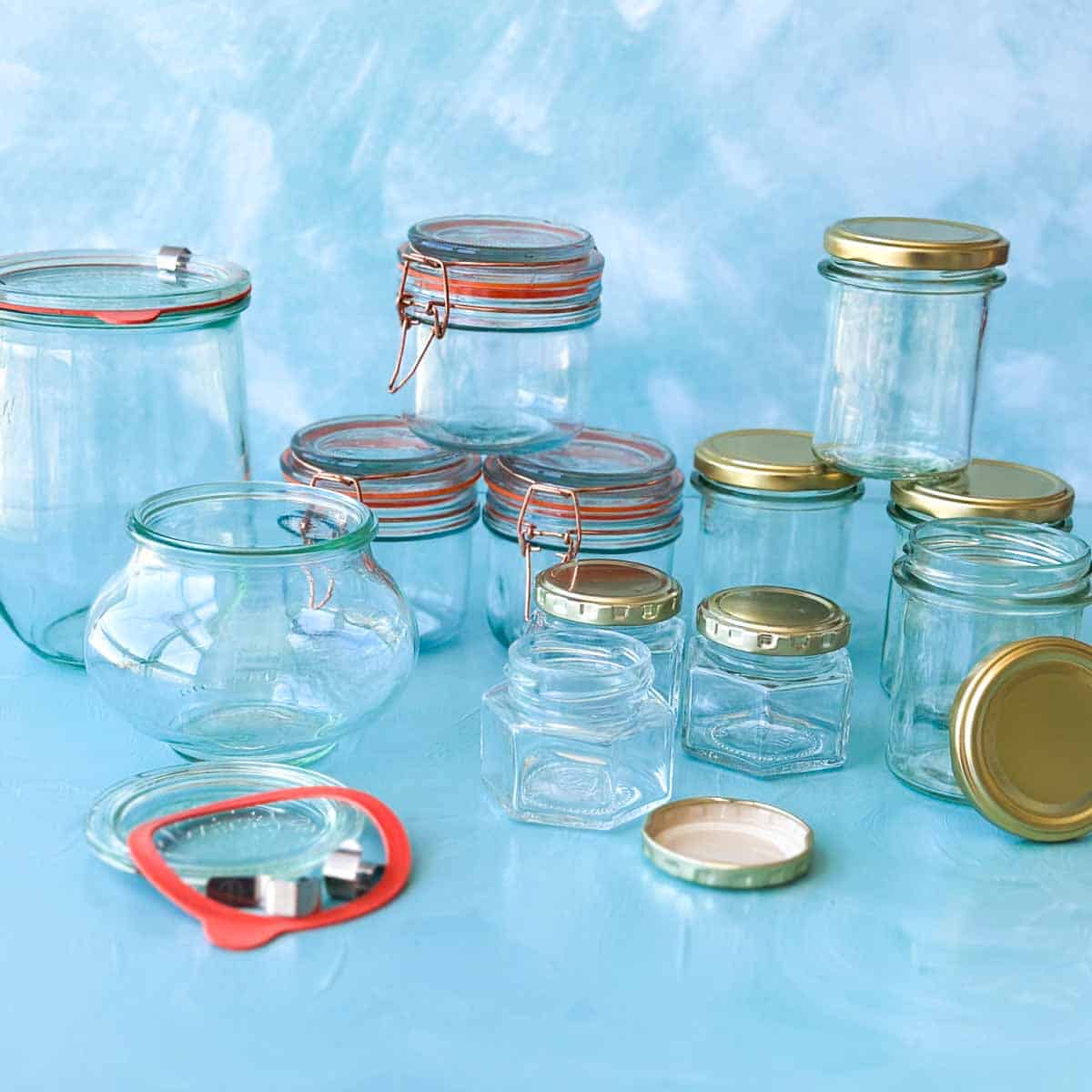 Clean glass jars, bottles, and lids arranged on a blue surface for sterilizing preserves and pickles.