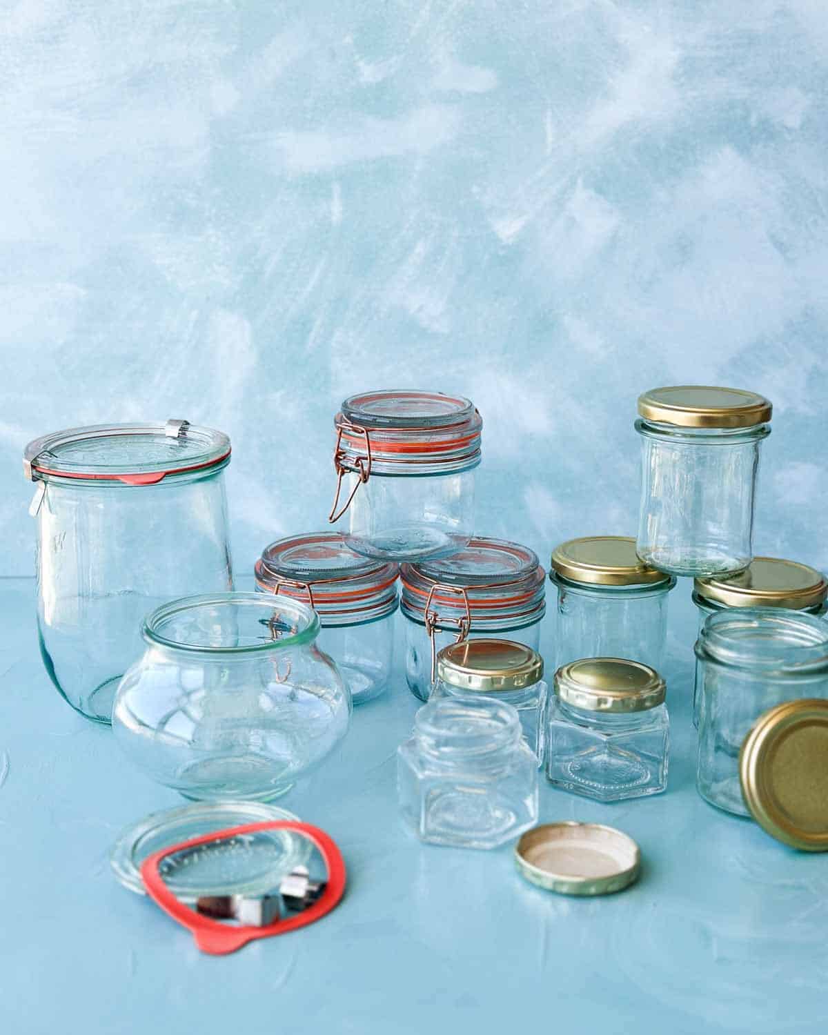 Wide view of empty glass jars, clip-top bottles, and metal lids ready for sterilizing before filling with jams or preserves.