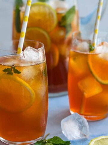 Close-up of refreshing lemon iced tea with ice, citrus slices, and mint leaves, served in tall glasses.
