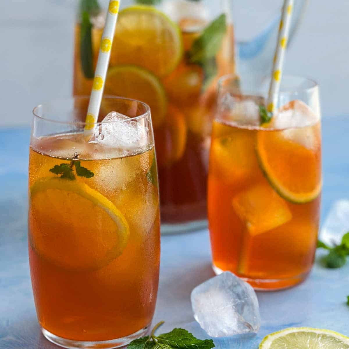 Close-up of refreshing lemon iced tea with ice, citrus slices, and mint leaves, served in tall glasses.