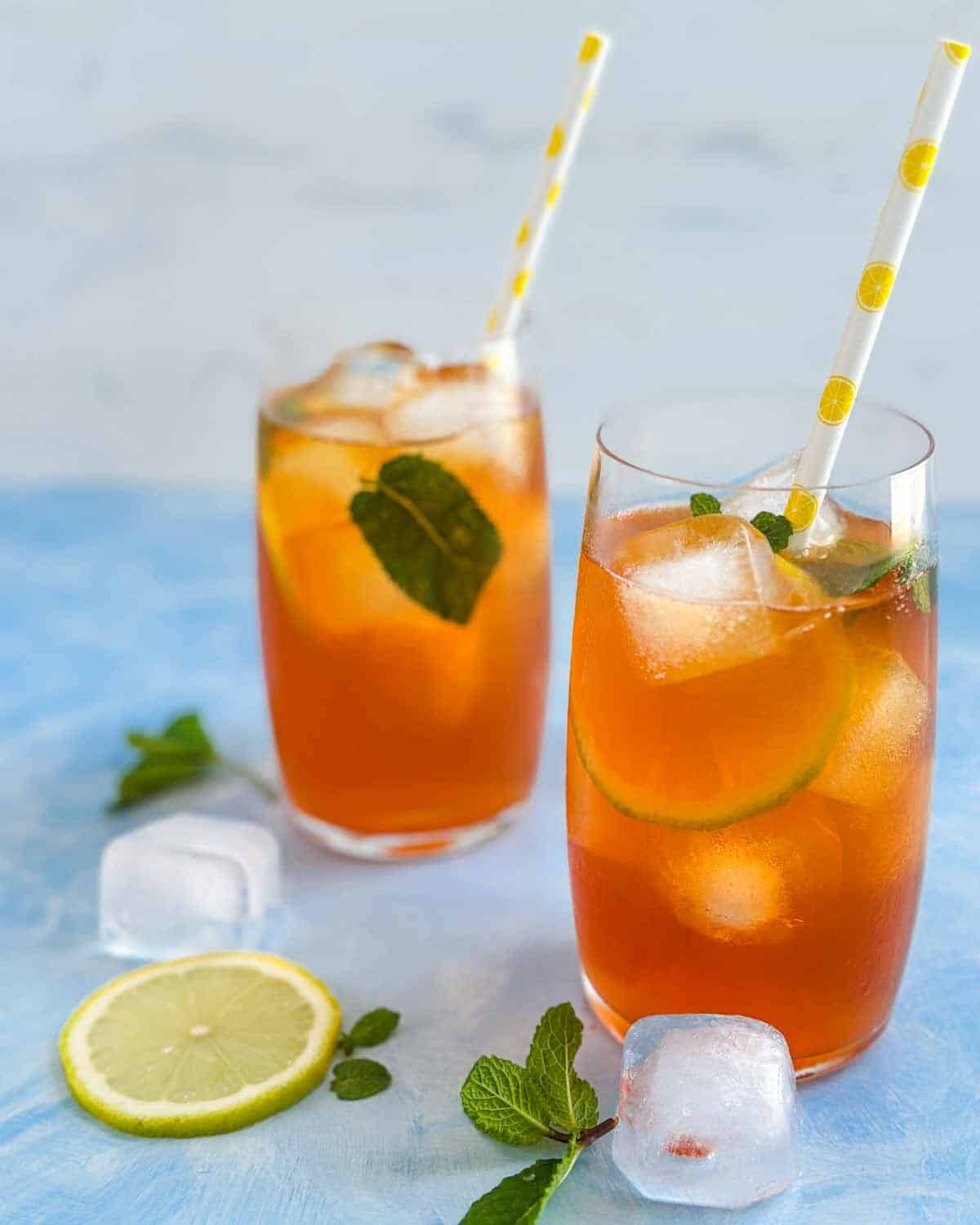 Close-up view of two glasses of lemon iced tea with ice, mint, and a lemon slice on the table.
