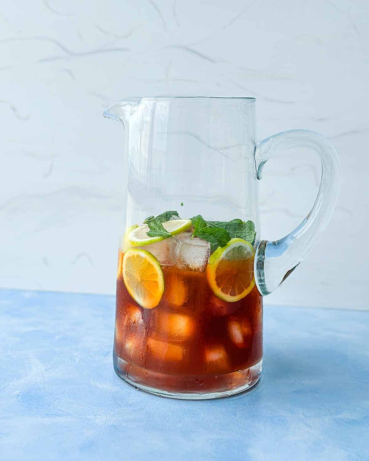 Glass pitcher filled with lemon iced tea, ice cubes, lemon slices, and fresh mint.