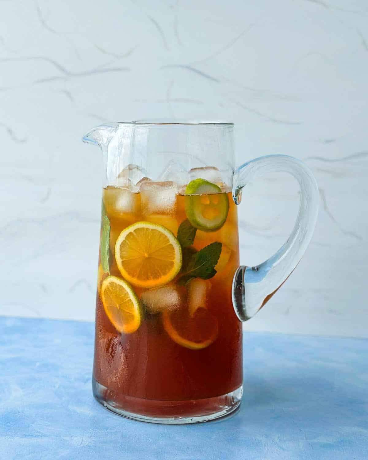 Close-up of a pitcher of lemon iced tea with ice, citrus slices, and mint ready to serve.
